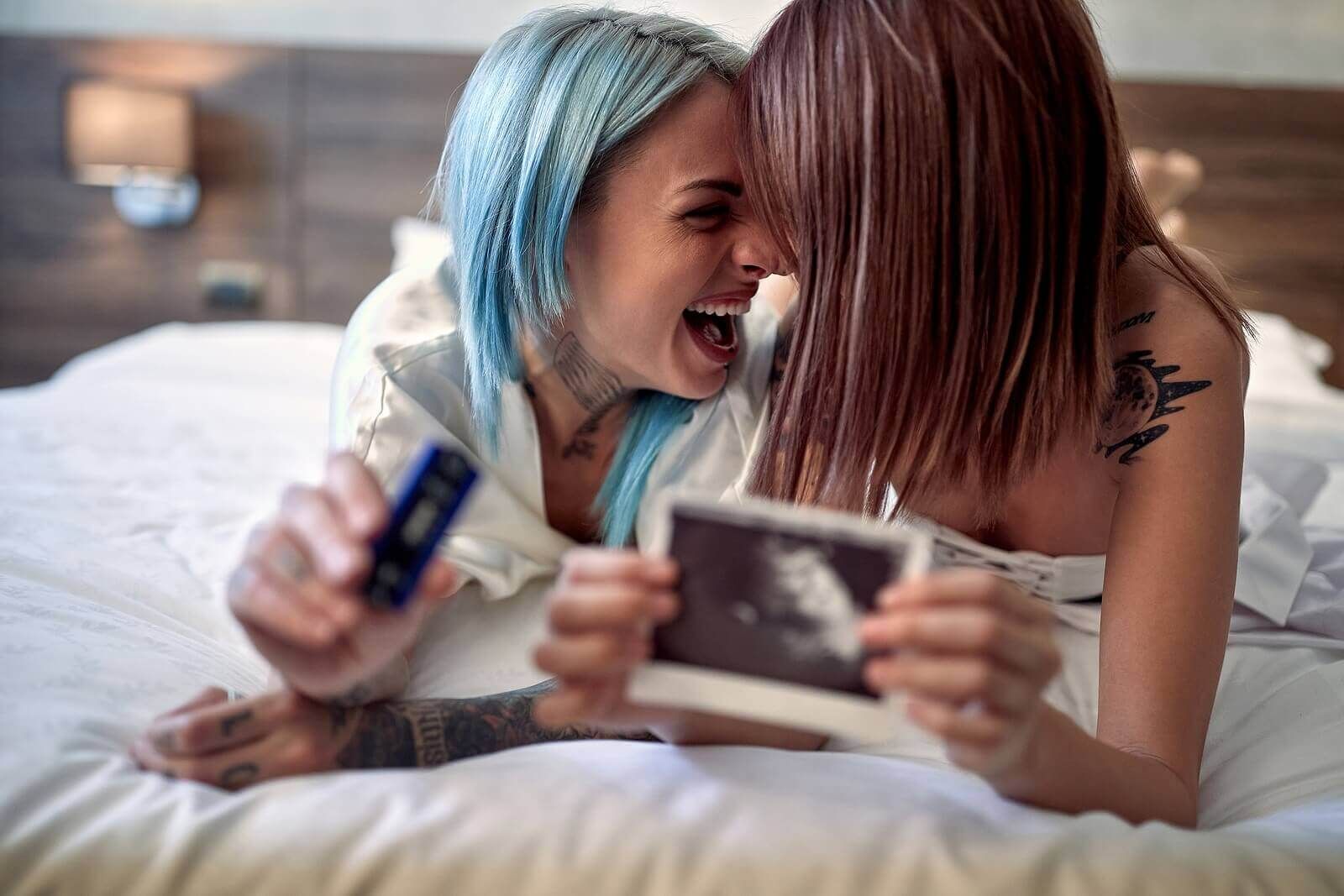 A lesbian couple laying on their bed celebrating their pregnancy representing an improved relationship built on the foundation of trust learned in the Hold Me Tight® workshops offered by Couples Workshops of Florida who serves couples in Florida, Alabama. Georgia, North Carolina and all over the world.