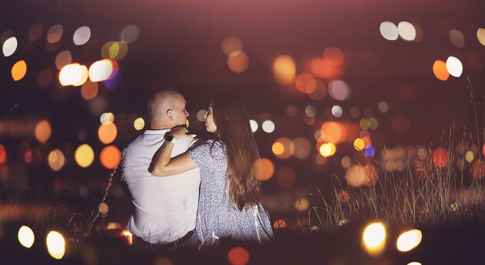 A couple sitting on a grassy area surrounded by flickering lights representing a couple who has strengthened their couples therapy through a Hold Me Tight® couples retreat  in Orlando, FL, Georgia, South Carolina, and beyond.