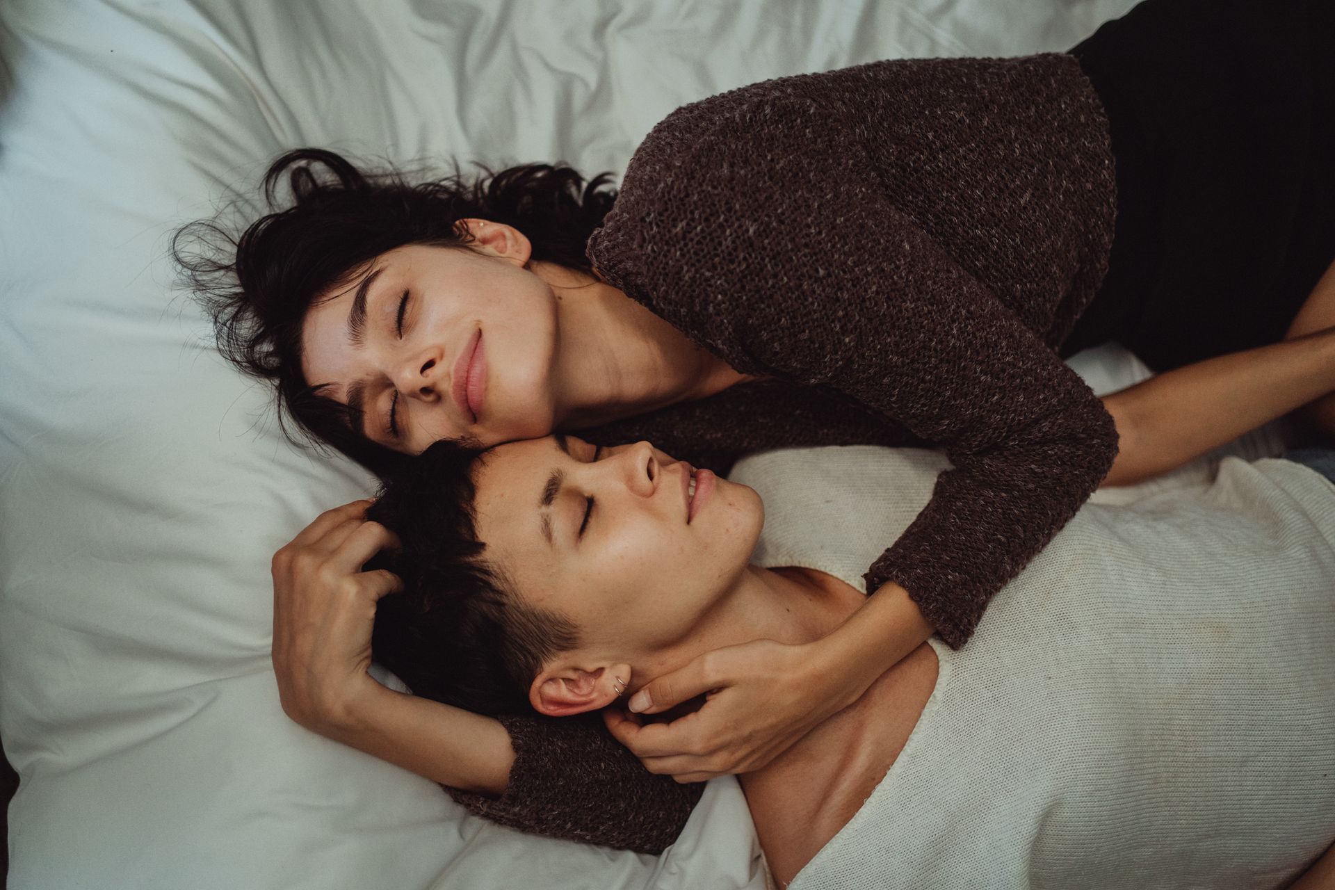 A lesbian couple snuggles on their bed representing the change in perception of how they view their relationship thanks to their participation in an Intimacy Workshop in Florida. Hold Me Tight® workshops are offered in Florida, Georgia, Virginia, and beyond. Working with us can improve the results of your couples therapy.