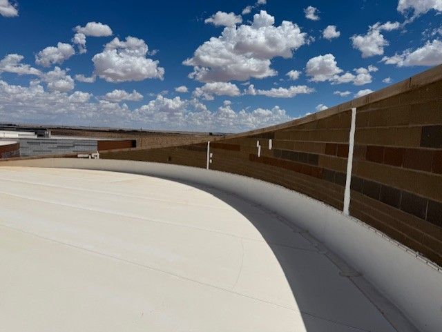 Curved rooftop edge with brick wall against a blue sky with clouds.