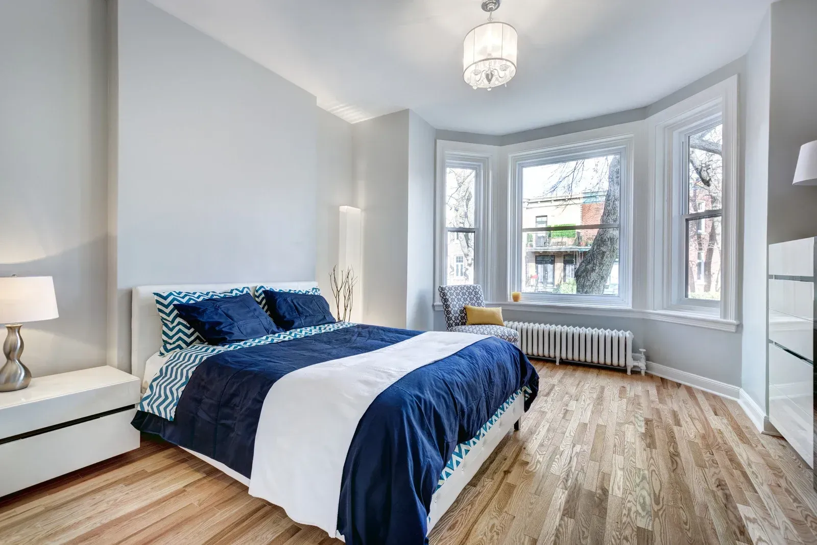 Bedroom with blue and white bedding, bay window, and hardwood floors.