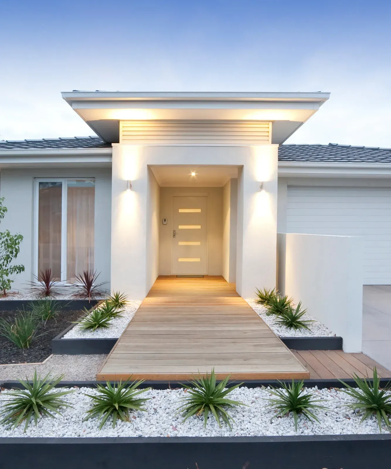 Modern home with a wooden walkway, white walls, and landscaping.