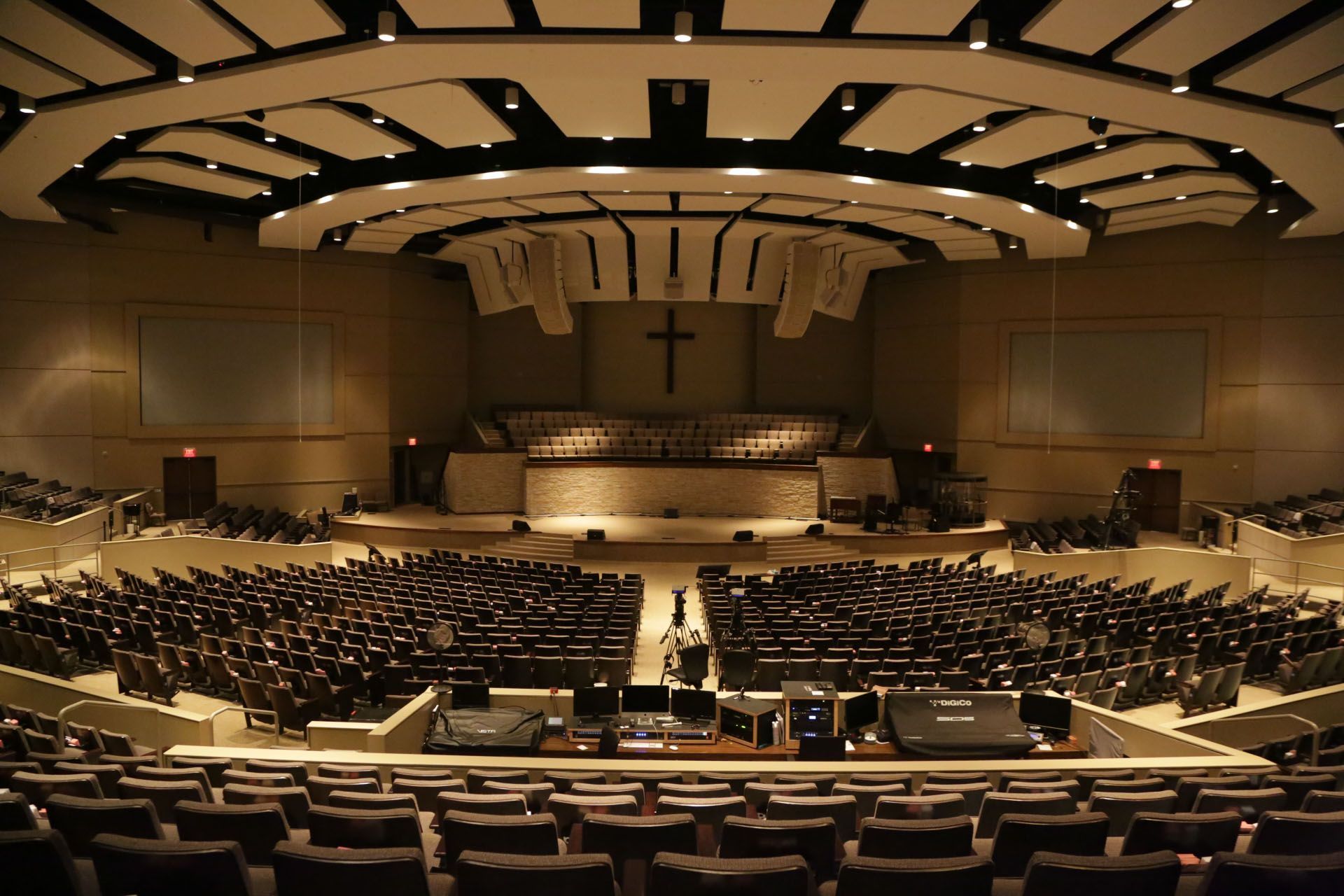 Auditorium with rows of seats facing a stage with a cross; warm lighting.