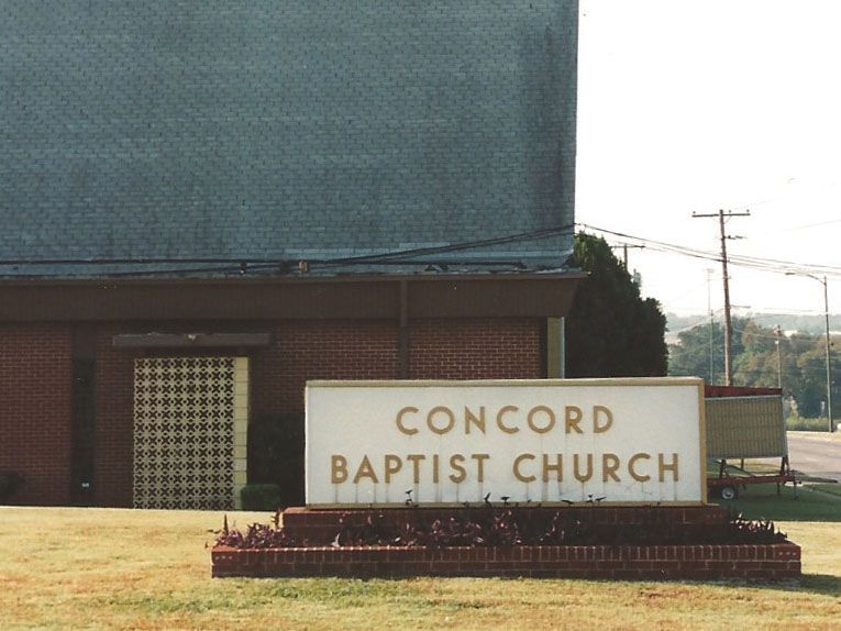 Concord Baptist Church sign in front of a brick building with a dark roof, on a grassy lawn.