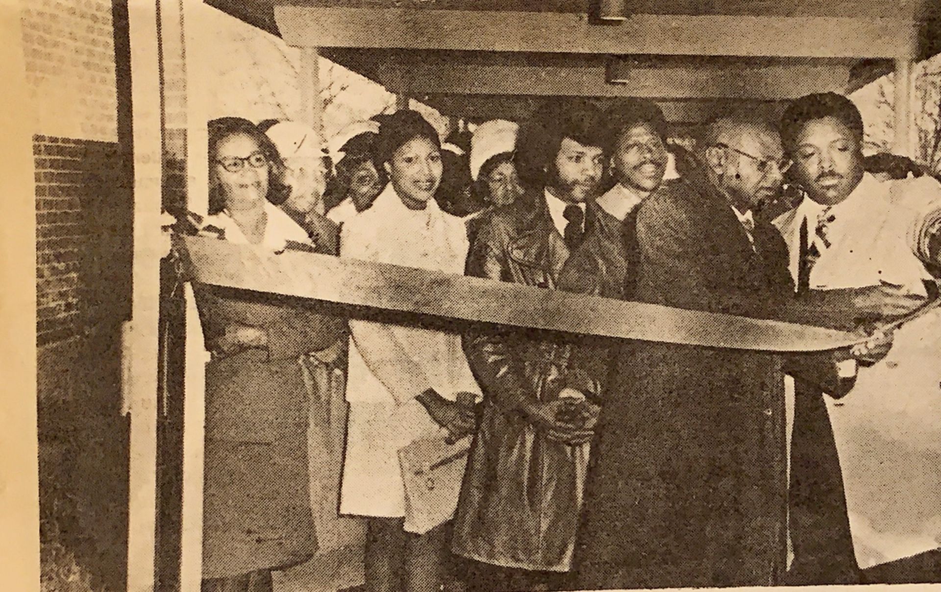 People cutting a ribbon at a building opening. Several Black men and women smile, celebrating.
