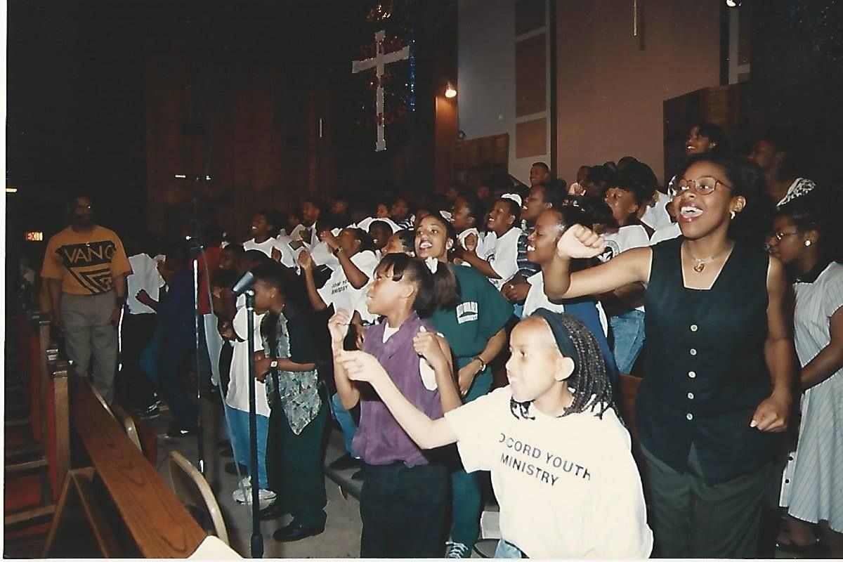 Choir in a church singing and raising hands. Cross on wall. People of color.