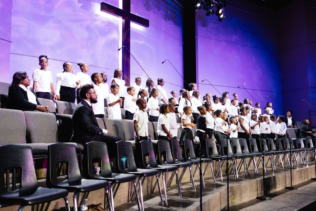 Choir singing on stage with cross backdrop, bathed in purple light.