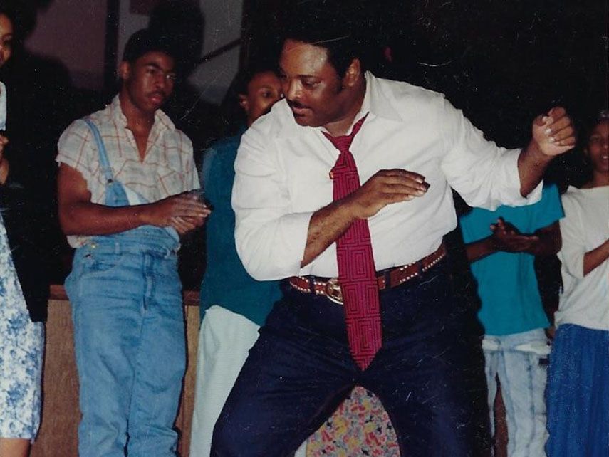 Man dancing with a red tie. People watch. Indoors.