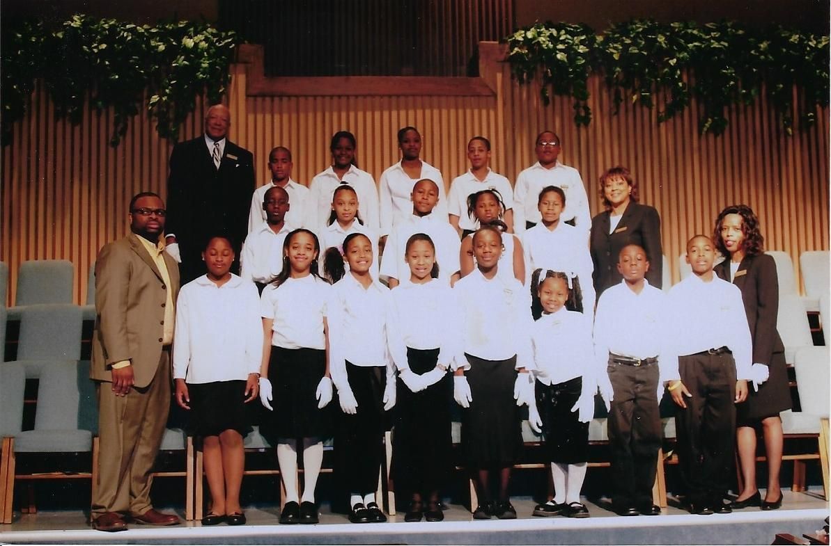Group photo of children and adults in a church setting, wearing white shirts and formal attire.