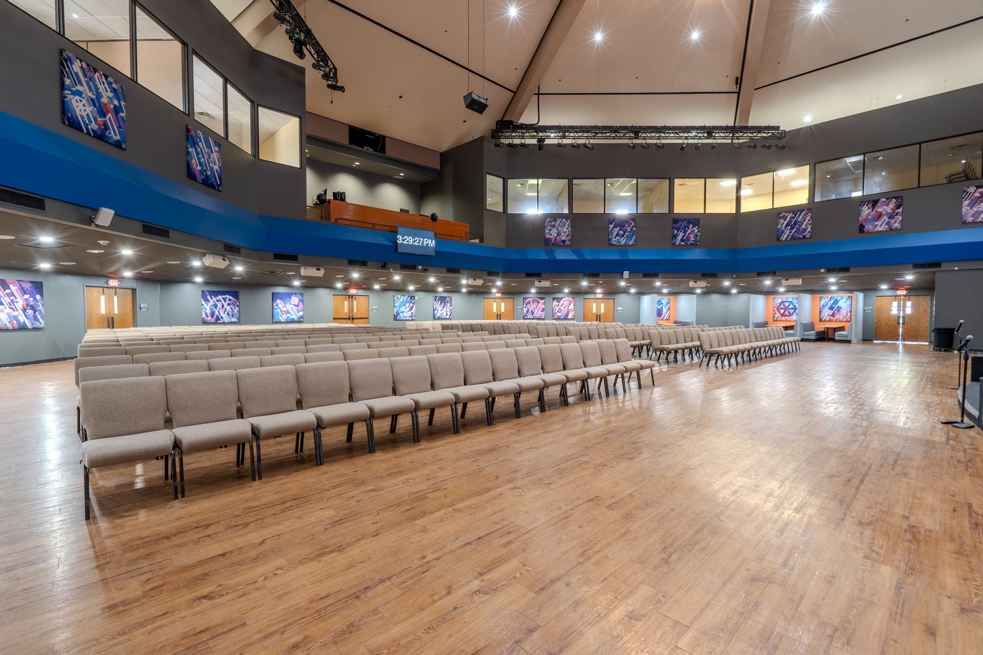 An auditorium with rows of chairs on a wooden floor, a blue balcony, and artwork on the walls.
