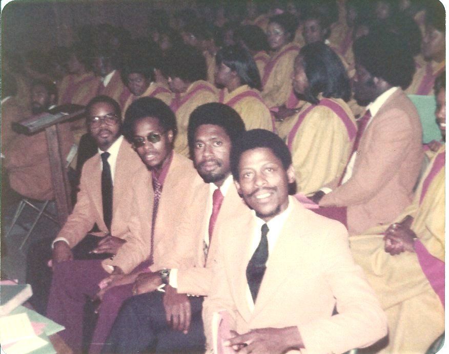 Men in light suits and ties with a gospel choir in the background, sepia-toned.