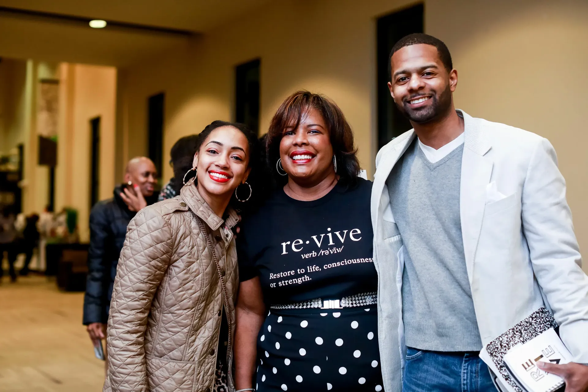 Three people smiling for a photo in a building hallway; a woman in a