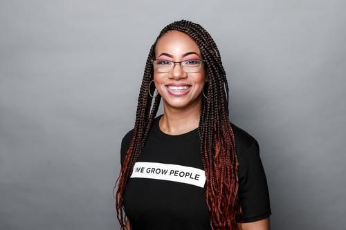 Woman with braided hair, glasses, smiles, wearing a black