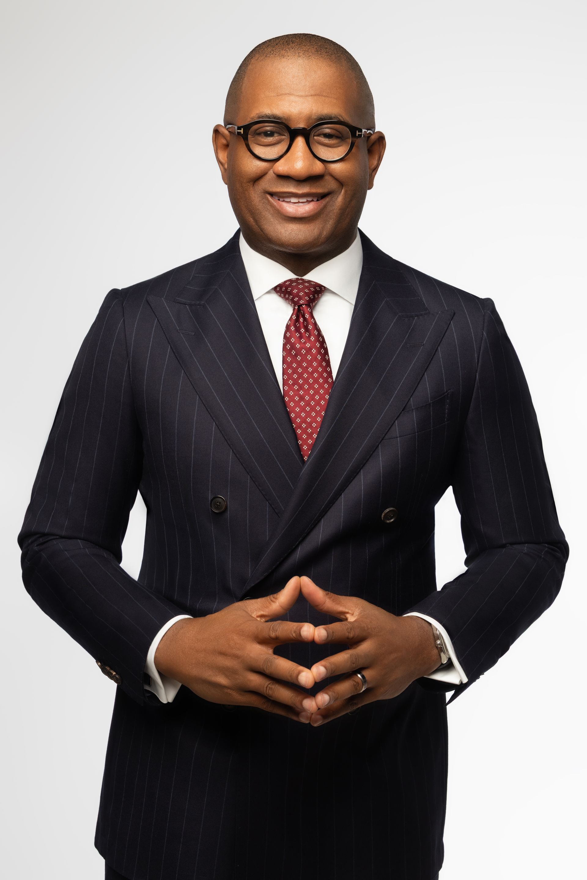 Pastor Carter in dark suit and red tie, smiling with hands clasped against a light background