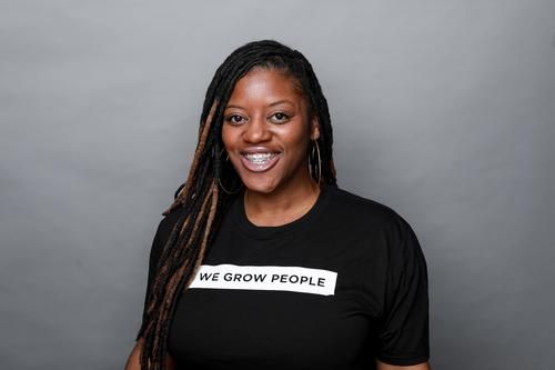 Smiling Black woman with long braids wearing a black t-shirt that says