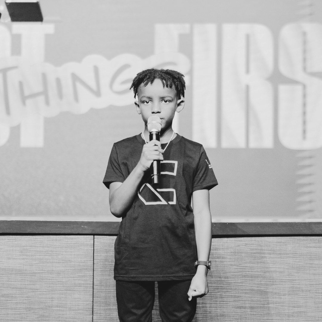 Young boy speaking into a microphone on a stage.