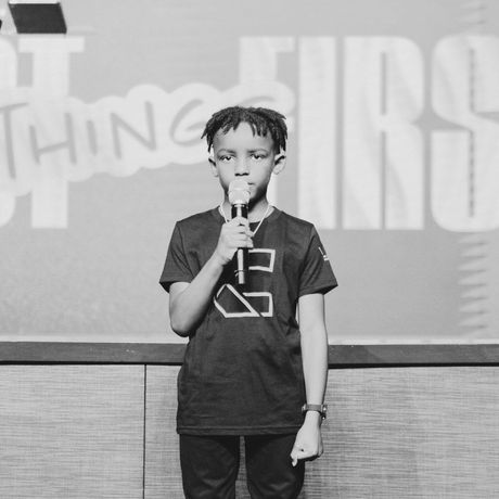 Young boy speaking into a microphone on a stage.