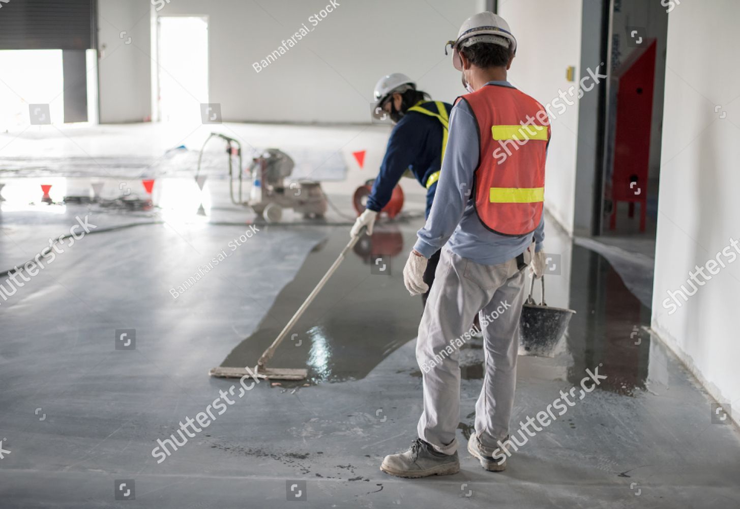Two construction workers are working on a concrete floor.