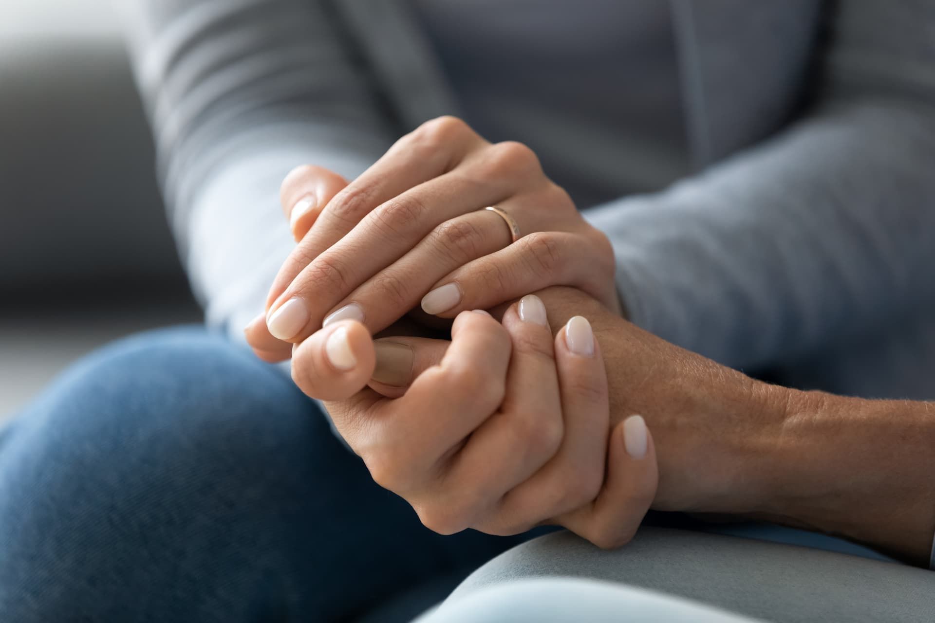 Two hands clasped together in a comforting gesture on a couch