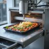 Una macchina automatizzata distribuisce la pasta su un vassoio con verdure cotte