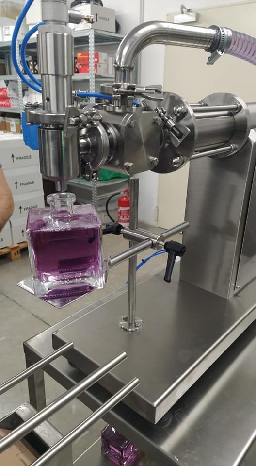 Macchina da laboratorio in acciaio inossidabile che versa un liquido viola in un becher di vetro su un tavolo di metallo.