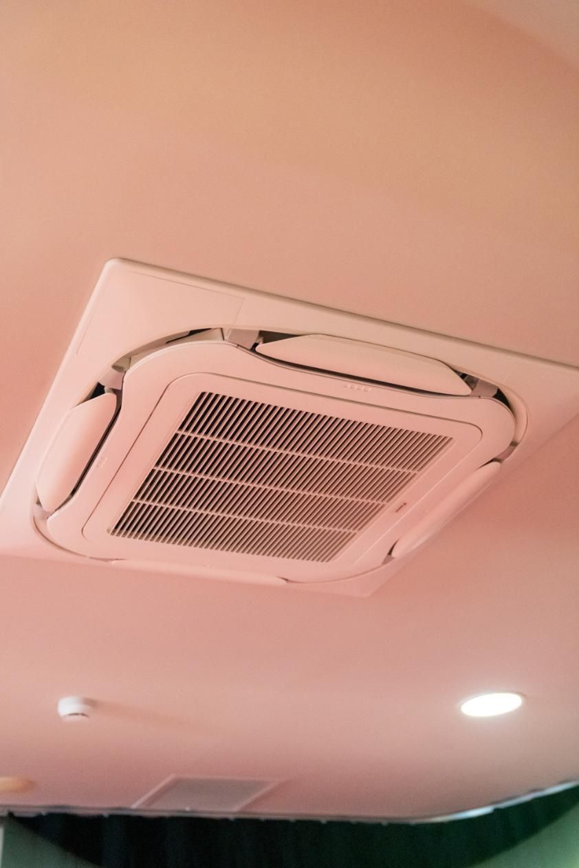 Ceiling-mounted air conditioning unit with a square, grid-like vent. It’s in a room with a pinkish ceiling — Gealy's Air-Conditioning, Refrigeration & Electrical in Noosaville, QLD