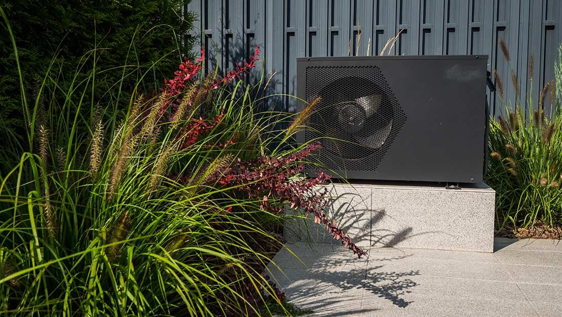 A Black Air Conditioner is Sitting on Top of a Concrete Block in a Garden
