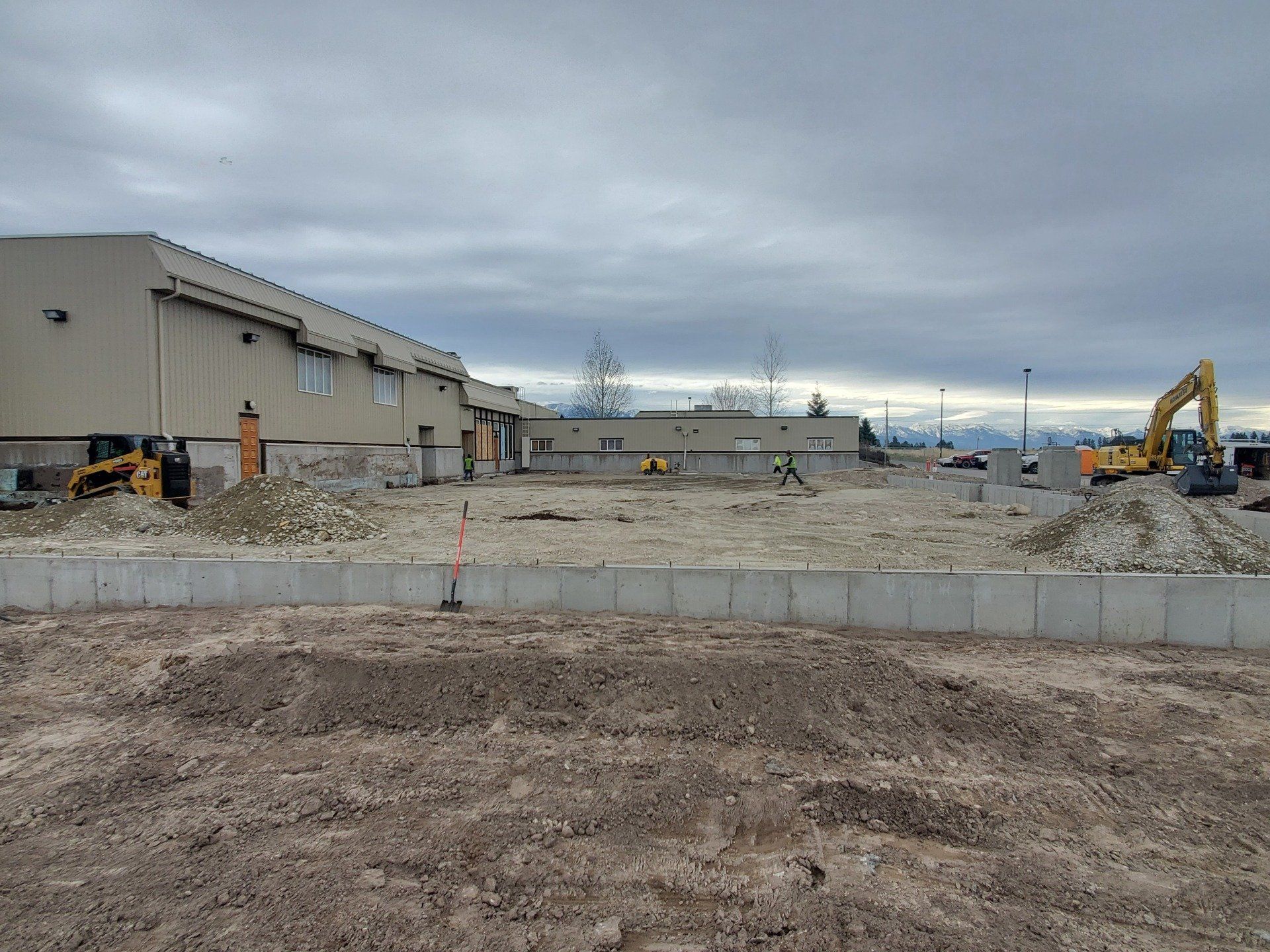 A construction site with a building in the background and a lot of dirt in the foreground.