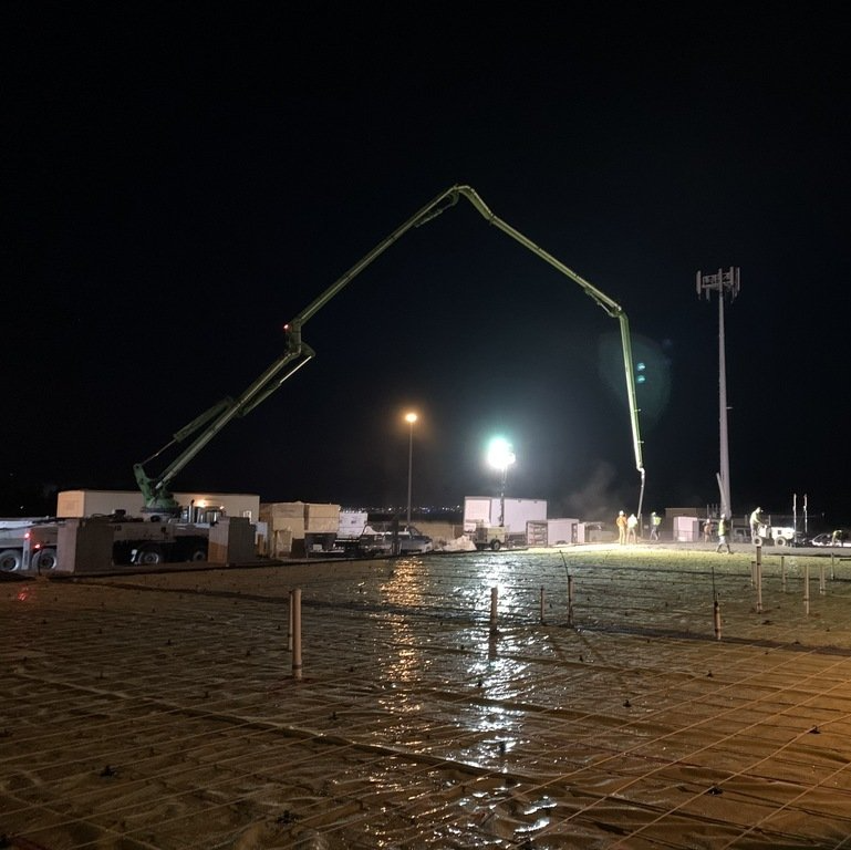 A construction site at night with a concrete pump in the foreground