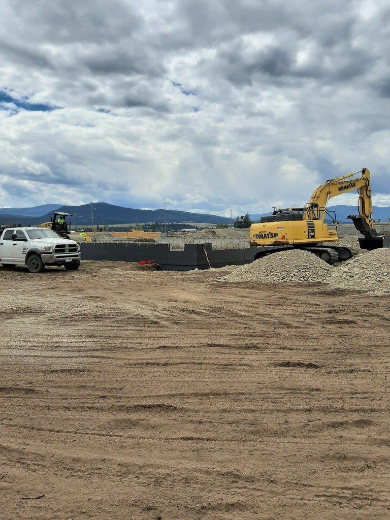 A white truck is parked in a dirt field next to a yellow excavator.
