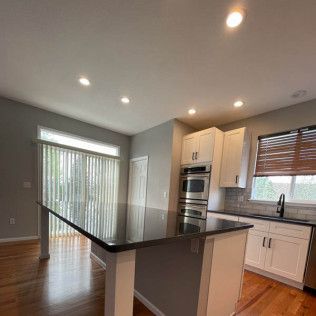 Modern kitchen with a black island, white cabinets, and wooden floors.