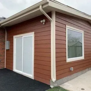 Brown siding on a building with a sliding door, window, and white trim.