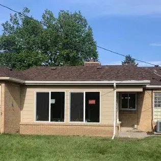 Rear view of a beige house with a brown roof and new windows.