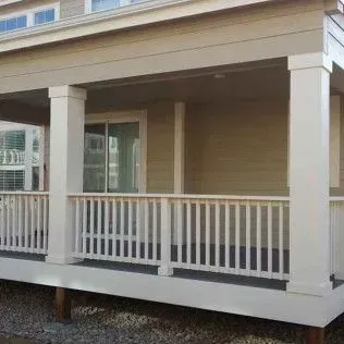 Covered porch with white pillars, railings, and tan siding.