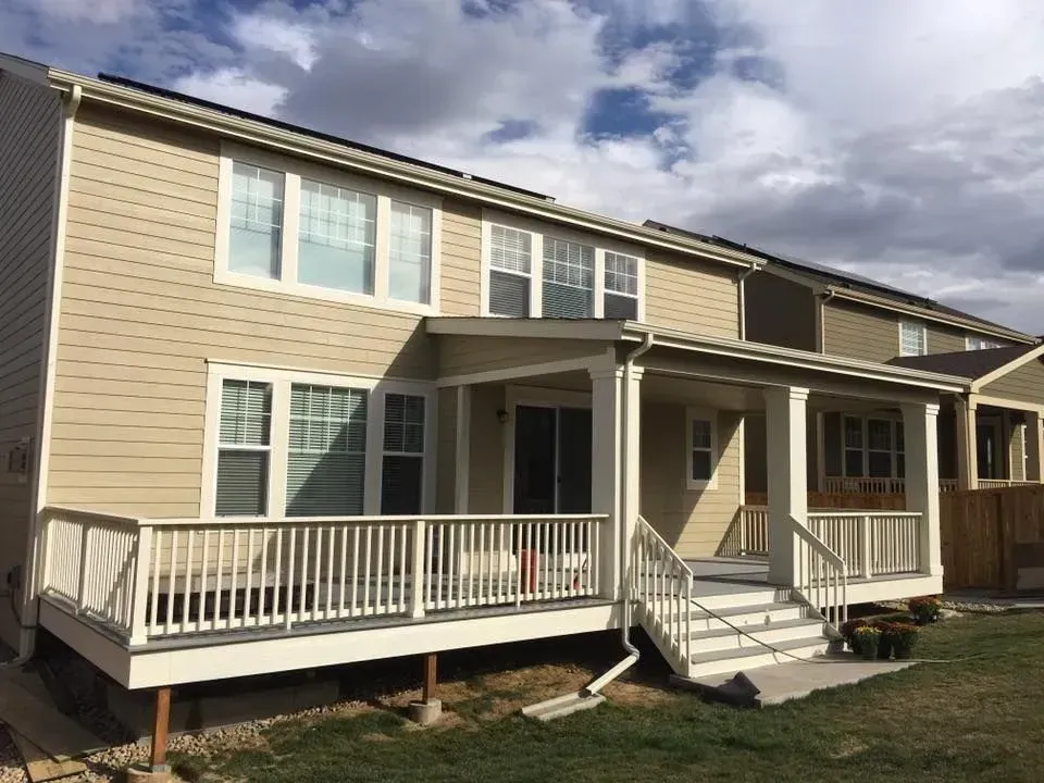 Tan house exterior with a deck, patio, and stairs, against a cloudy sky.