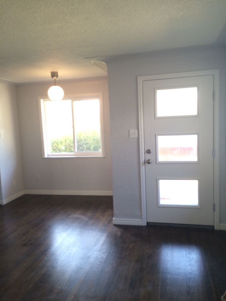 Interior view: gray walls, white door with three windows, dark wood floor, bright window, and a round light.