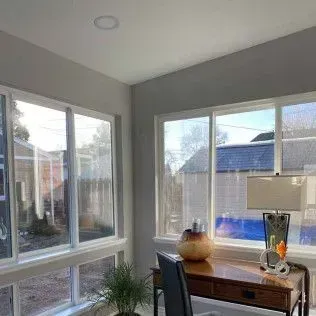 Sunlit corner room with desk and windows. A lamp sits on the desk. A plant is in the foreground.