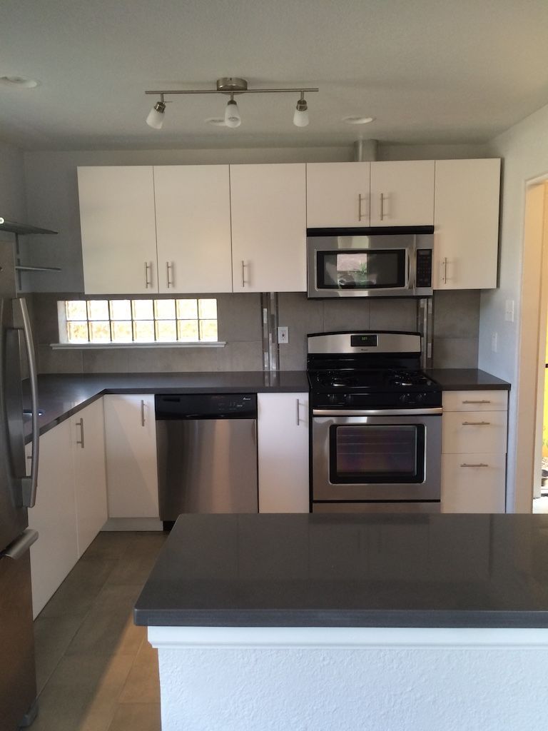 Modern kitchen with white cabinets, stainless steel appliances, dark countertop, and overhead lighting.