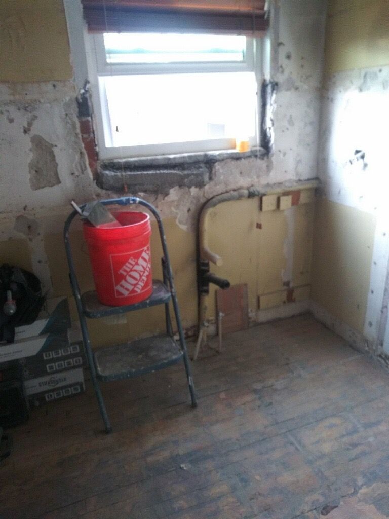 A room under renovation; exposed walls, ladder with bucket near a window.