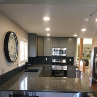 Modern kitchen with gray cabinets, black countertops, and a large clock on the wall.
