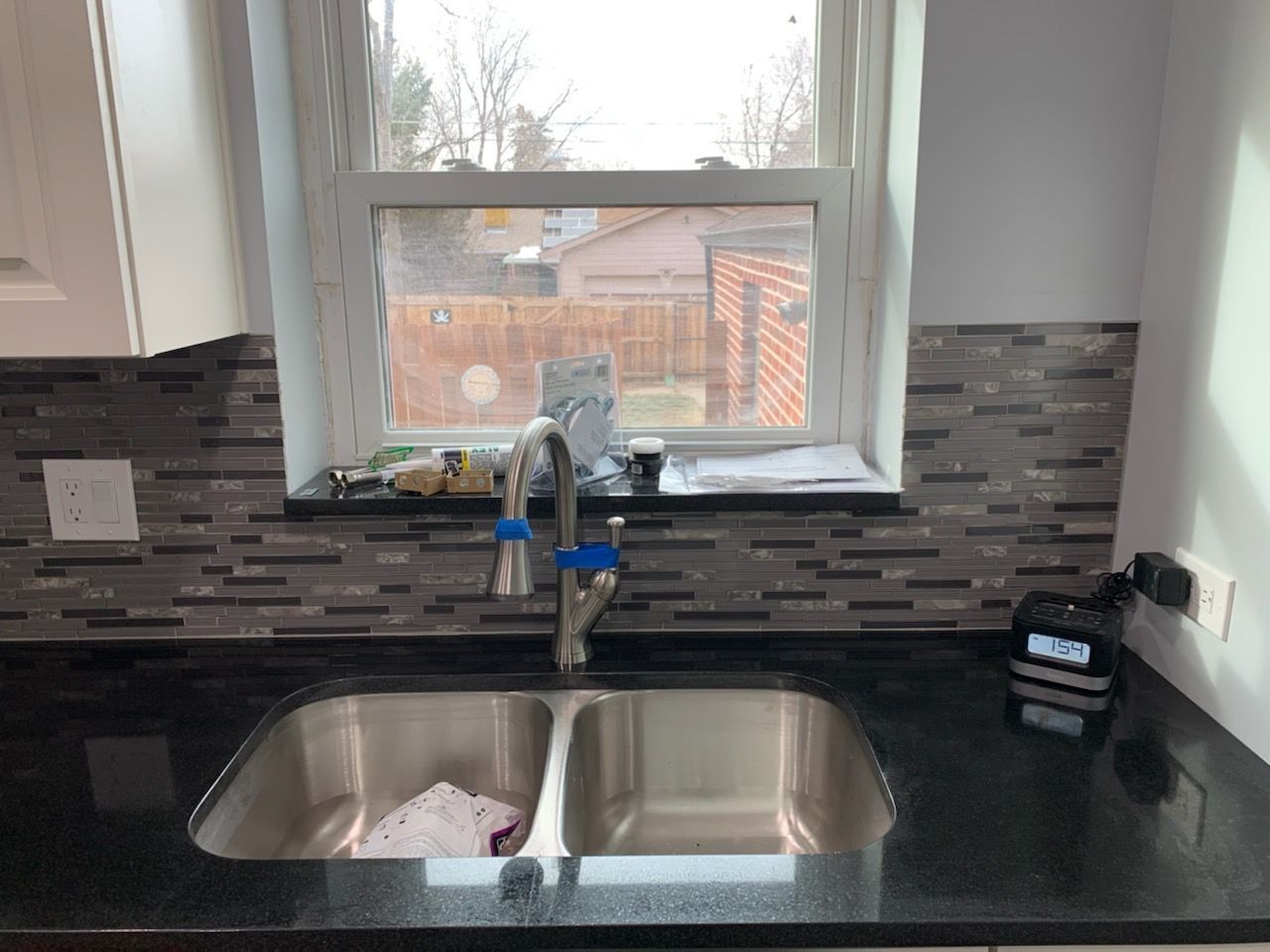 Kitchen sink with dark countertops and tiled backsplash under a window.