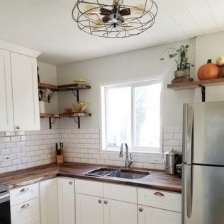 Cozy kitchen with white cabinets, butcher block counters, subway tile, open shelves, and a stainless steel refrigerator.
