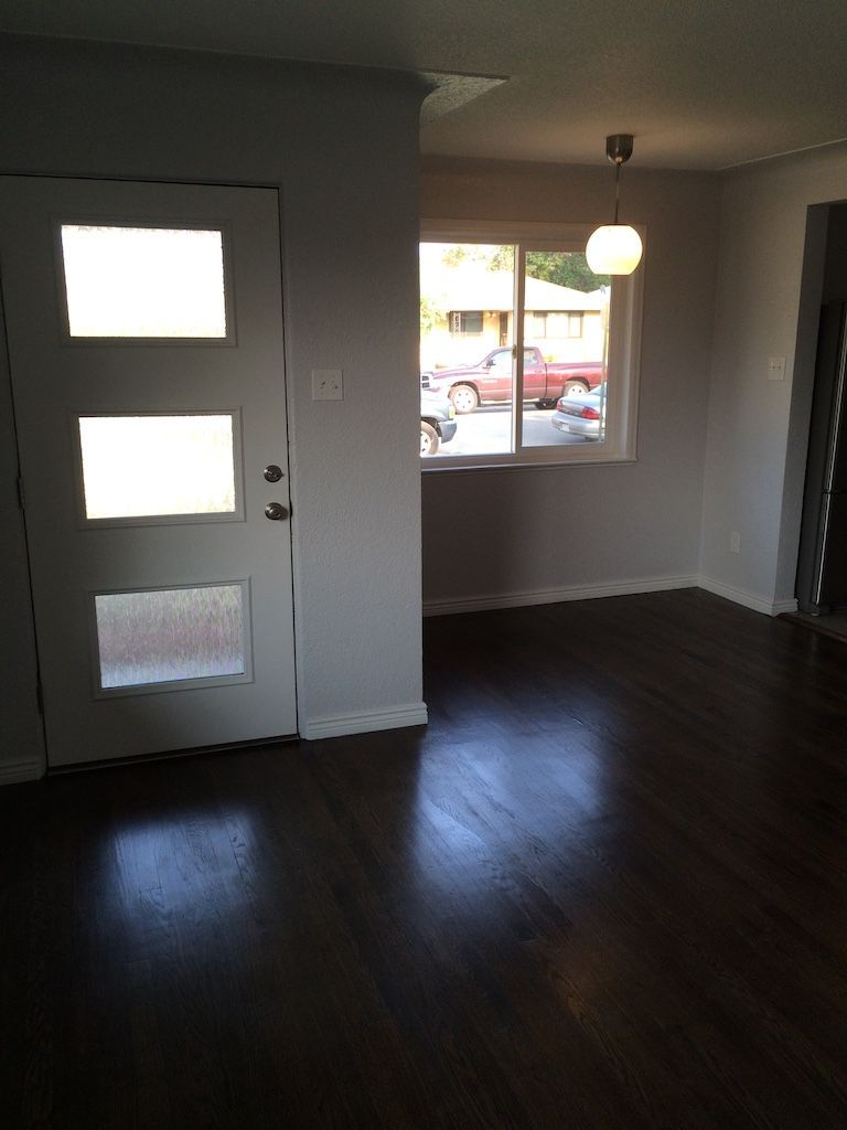 Interior view of a room with dark wood floors, light gray walls, a window, and a door with glass panels.
