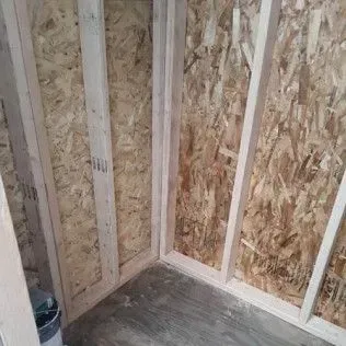 Framed interior corner; oriented strand board walls, light wood framing, gray concrete floor.