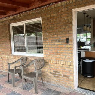 Two plastic chairs sit near a window and open doorway on a brick patio.