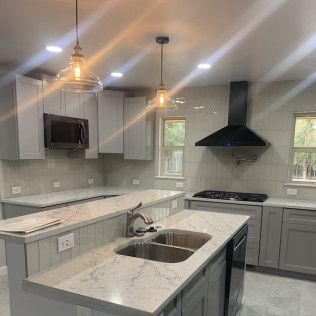 Modern kitchen with light gray cabinets, quartz countertops, and stainless steel appliances.