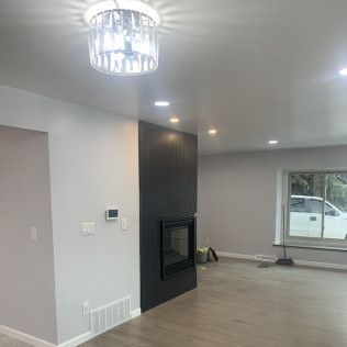 A living room with a black fireplace, recessed lighting, and a crystal ceiling light. Gray walls and flooring.