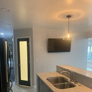Kitchen with a sink, countertop, black door, and a TV on the wall. A light fixture hangs from the ceiling.