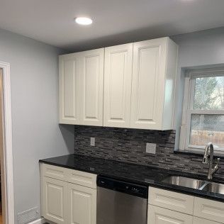 Kitchen with white cabinets, dark countertops, backsplash, and stainless steel sink and appliances.