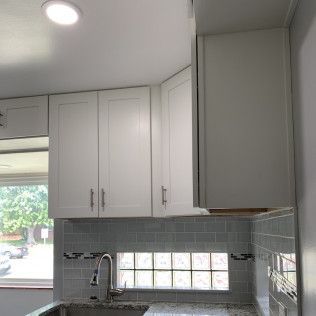 White kitchen cabinets above a sink, with a glass block window and grey tile backsplash.